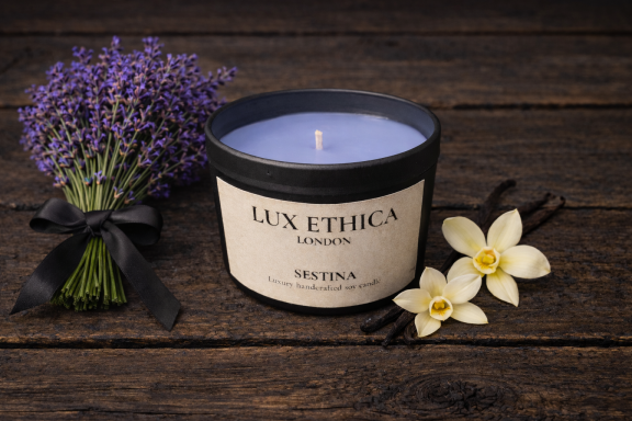 Sestina A lavender candle beside fresh lavender and two white flowers on a wooden surface.