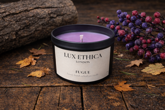 Fugue Purple candle in a black container, surrounded by autumn leaves and decorative berries.